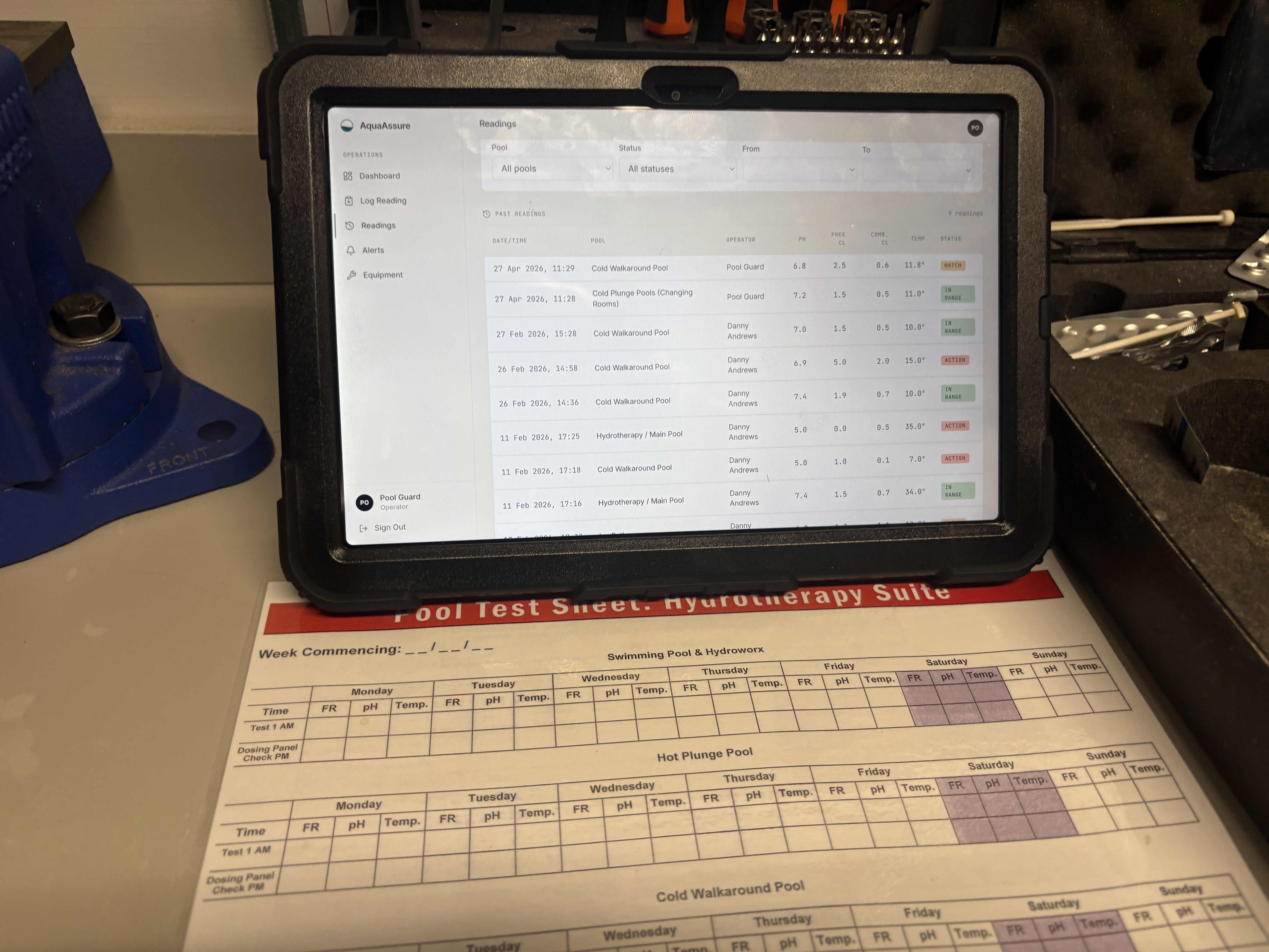 AquaAssure log reading screen on a tablet with a paper pool test sheet visible behind it